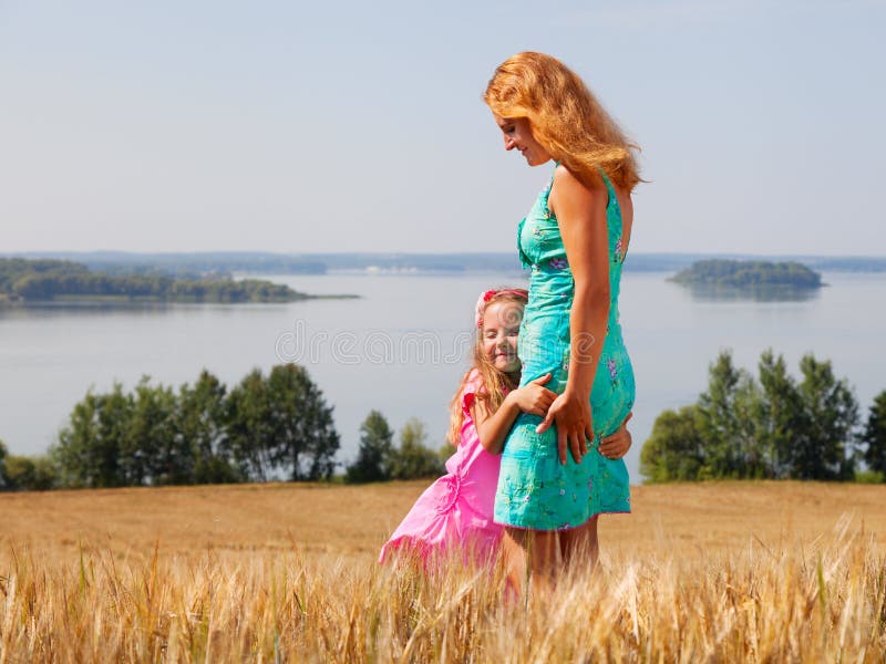 Little girl hugging her mother in a wheat field near lake