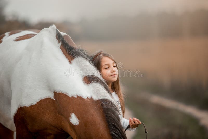 Little girl in indian style with pinto pony in a summer field in sunny evening. Little girl in indian style with pinto pony in a summer field in sunny evening