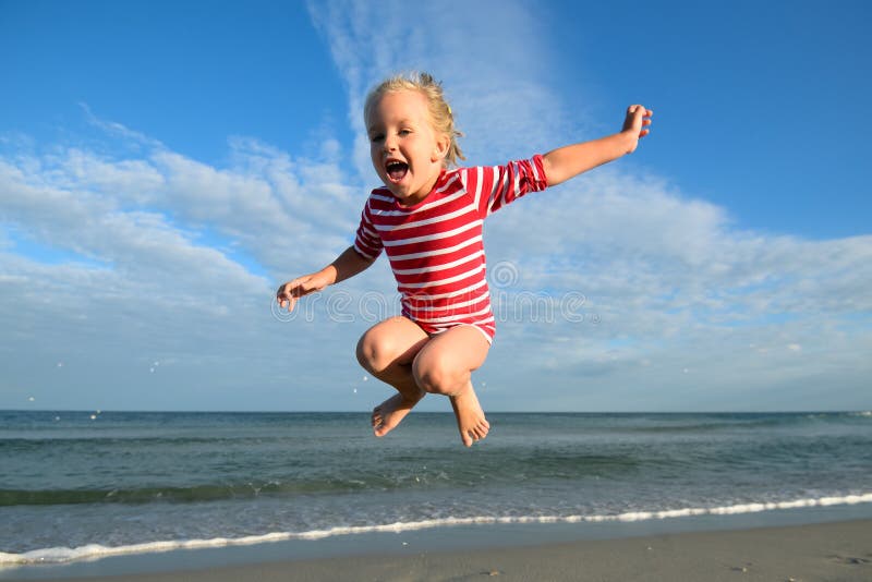 Little girl jumping and hovering in the air on the background of blue sky and summer sea. Happy child girl playing at beach and