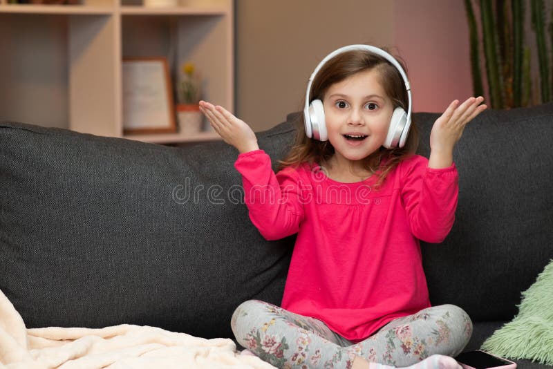 Little Girl Listens To Music On Wireless Headphones. Funny Little Girl Dancing, Singing And Moving To Rhythm. Kid