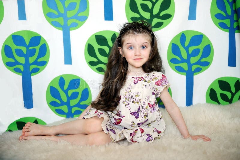 Little girl with long hair in colorful dress sits