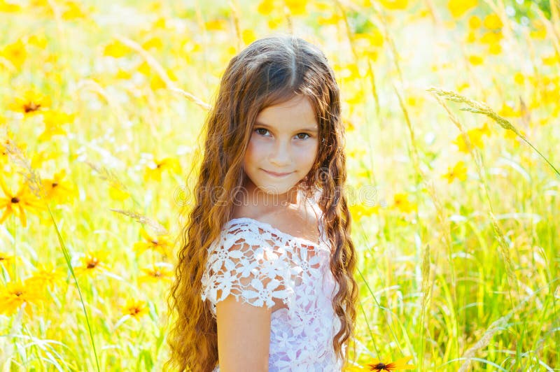 Little girl with long hair in a white dress rejoices in a field with flowers