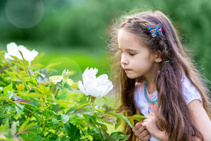 Little girl looking into the flower in green garden or park