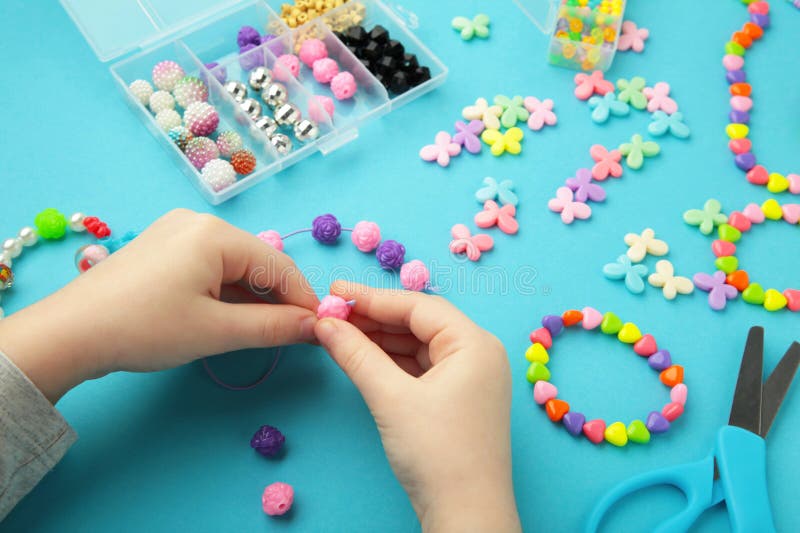 Little girl made bracelets on blue background. Kids handmade beaded jewelry. DIY bracelet beads