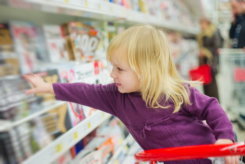 Little girl at magazines section in supermarket