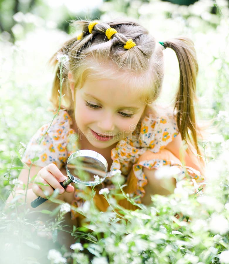 Little girl with magnifying glass looks at flower