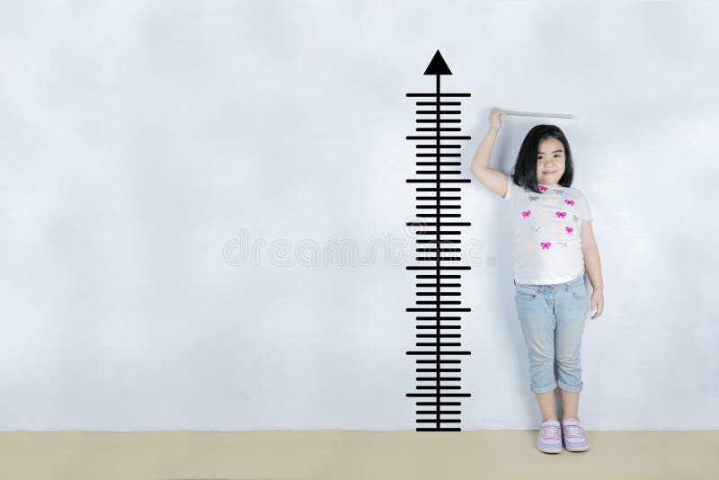 Little girl measuring height near white wall