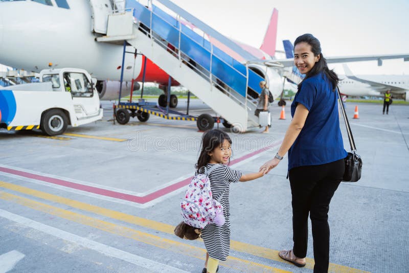 Little girl and mother holding hands walk towards the plane