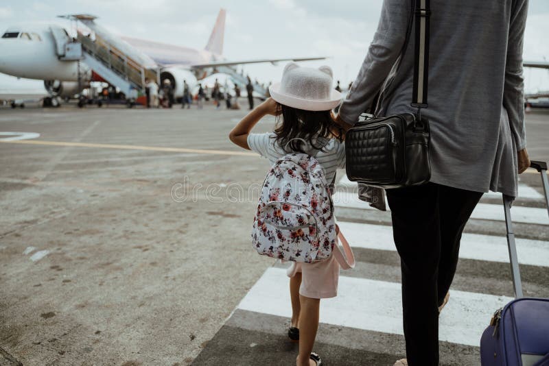 Little girl and mother holding hands walk towards the plane