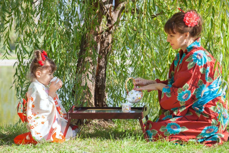 Little girl with mother in kimono sitting beside the tea table