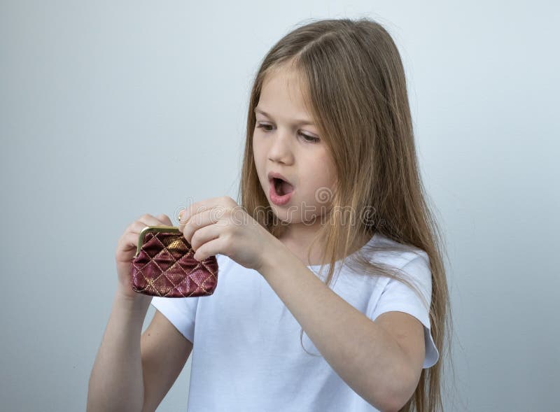 Little girl opens the wallet, sees that it is empty and surprised. Learning financial responsibility and projecting savings. Saving money for future, investment concept. Pocket money for children.