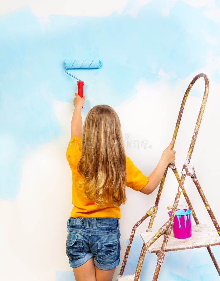 Little girl paints the wall standing on a ladder