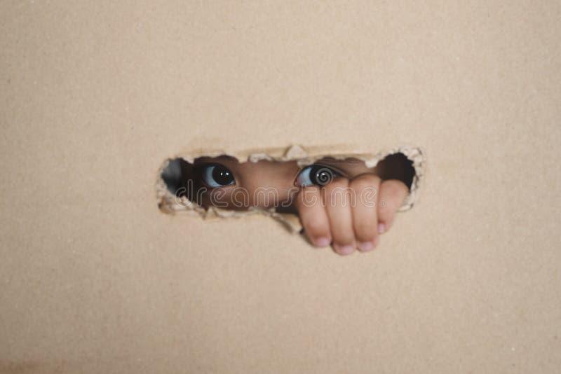 Little girl peeking from a hole on cardboard box selective focus on her eye.