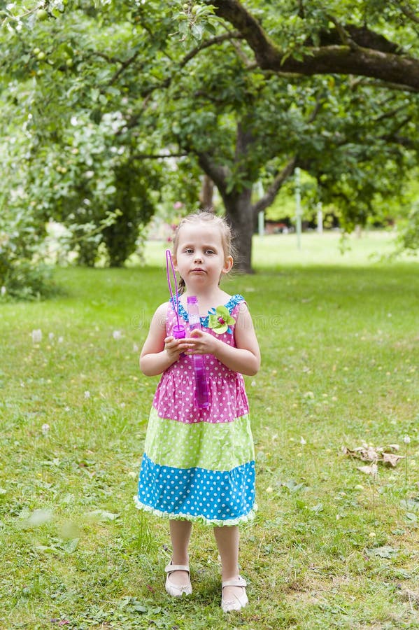 Little girl with pigtails in a colorful dress pensively standing in the park with soap bubbles royalty free stock photography Little girl with pigtails in a colorful dress pensively standing in the park with soap bubbles royalty free stock photography