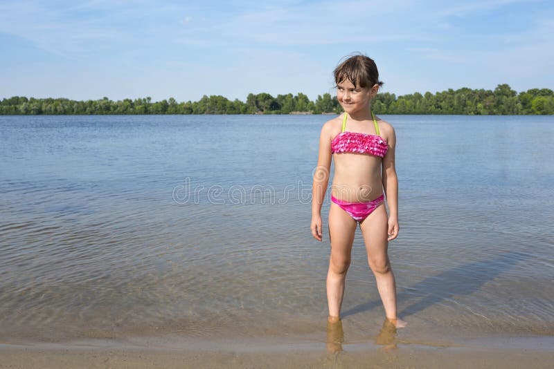 Little girl in a pink bathing suit on the river, on a sunny, warm day