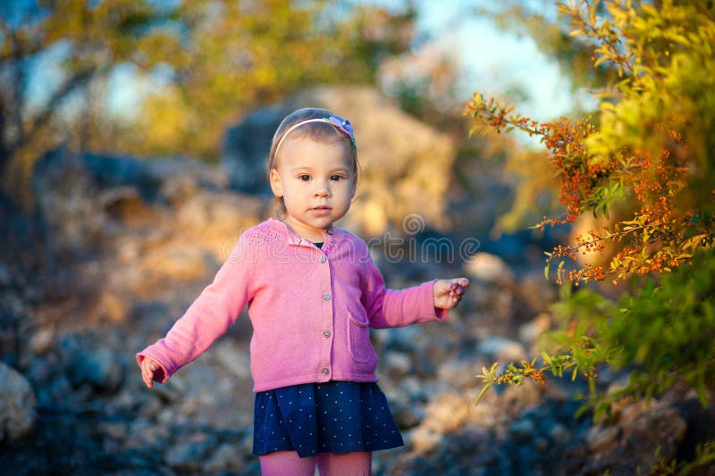 Little girl in a pink jacket touch pen orange berries on the bush.