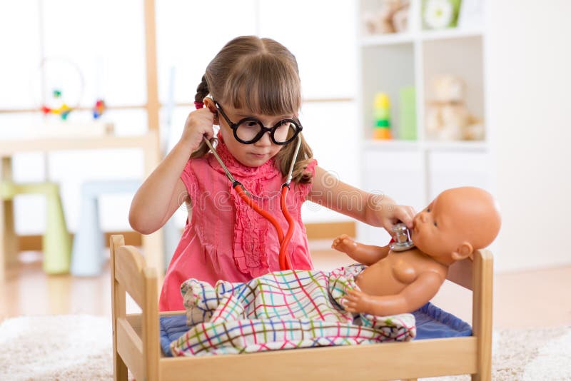 Little girl playing the doctor with her newborn baby doll in room