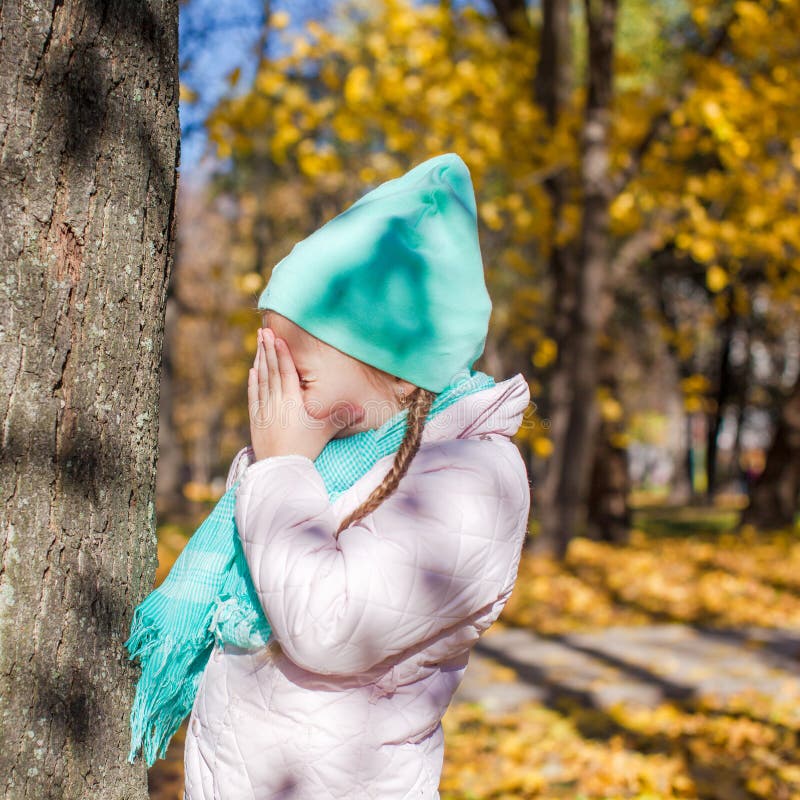 Little girl playing hide and seek in the autumn forest. This image has attached release.