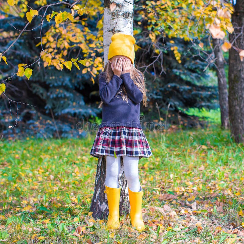 Little girl playing hide and seek near the tree in autumn forest. Little girl playing hide and seek near the tree in autumn forest