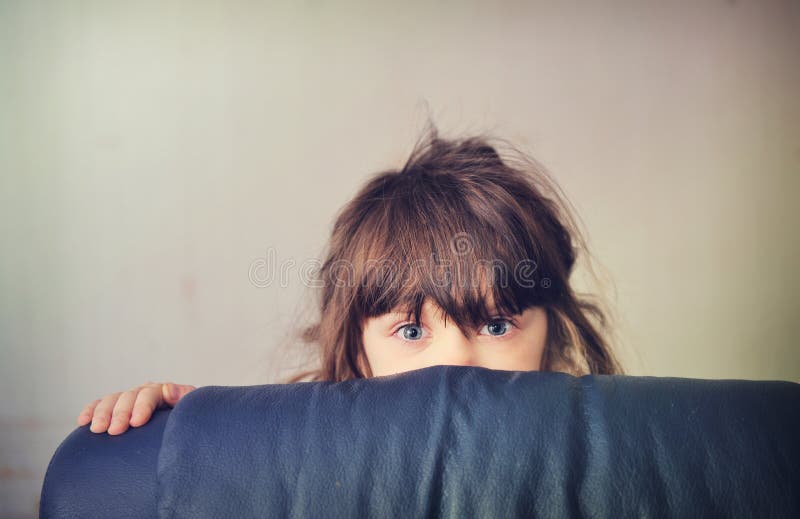 Little girl playing hide and seek behind the sofa