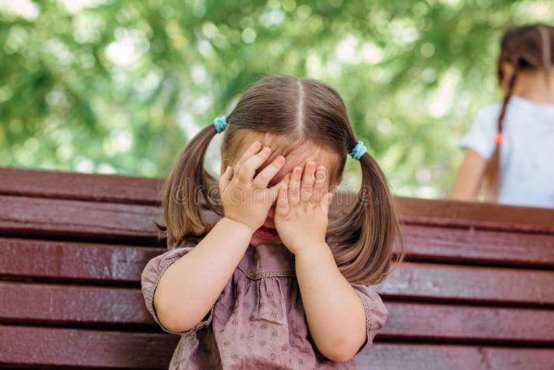 Little girl is playing hide-and-seek hiding face in park