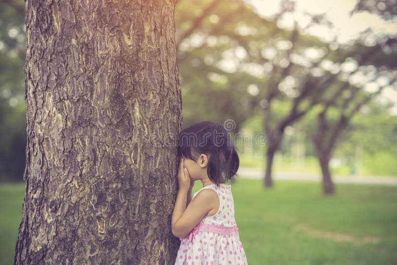 Little girl is playing hide-and-seek hiding face in the park.Vintage color