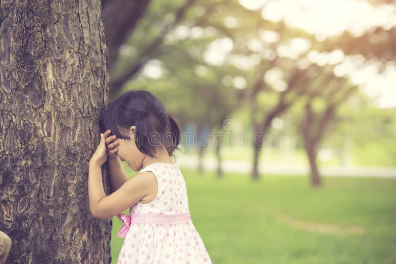 Little girl is playing hide-and-seek hiding face in the park.Vintage color