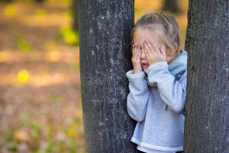 Little girl playing hide and seek in autumn forest outdoors. Little girl playing hide and seek in autumn forest outdoors