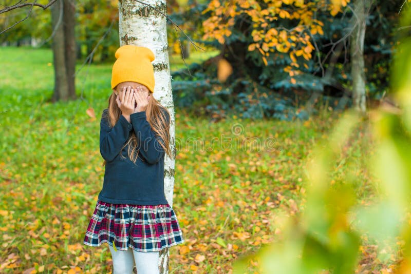 Little girl playing hide and seek in autumn forest outdoors. Little girl playing hide and seek in autumn forest outdoors