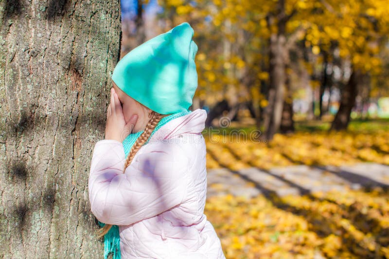 Little girl playing hide and seek near the tree in autumn park. This image has attached release.