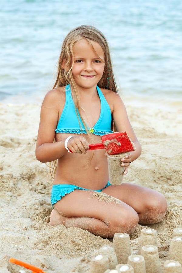 Little girl playing with sand on the beach - building little towers