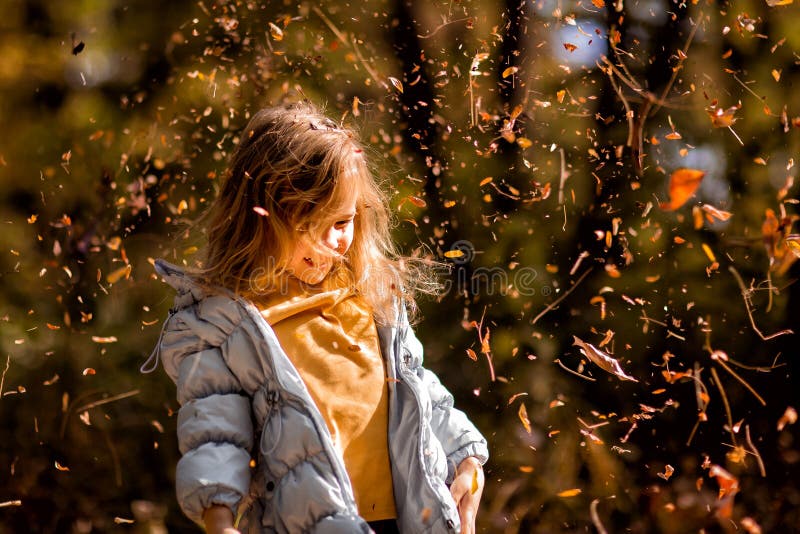 Little girl plays with dry yellow leaves in autumn Park