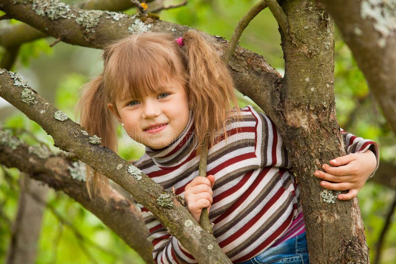 Little girl posing sitting on a tree in the garden