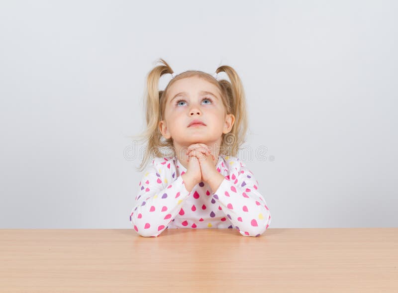 Little girl praying and looking up. Sitting at the table.