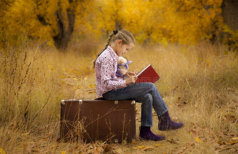 Little girl is reading a book in autumn