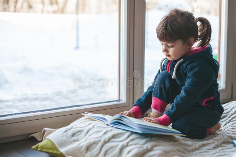 Little girl reading a book near the window