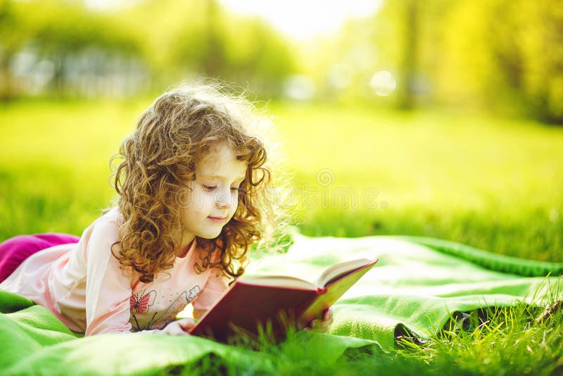 Little girl reading a book in the spring park