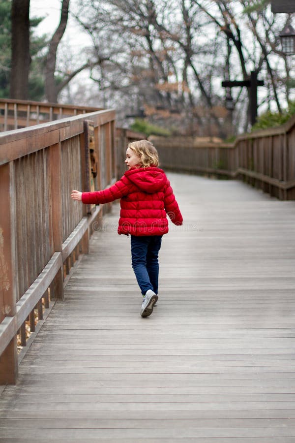 A little girl in a red jacket walks down the road touching the fence royalty free stock image A little girl in a red jacket walks down the road touching the fence royalty free stock image