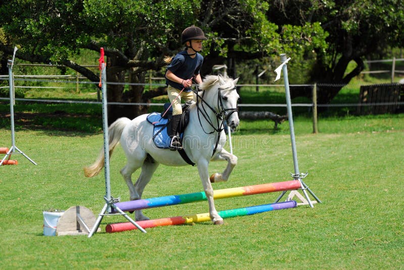 Joven caucásico saltando el curso su blanco pequeno poni.