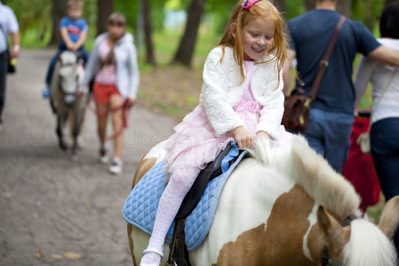 Little girl riding on a pony in a city park stock images Little girl riding on a pony in a city park stock images