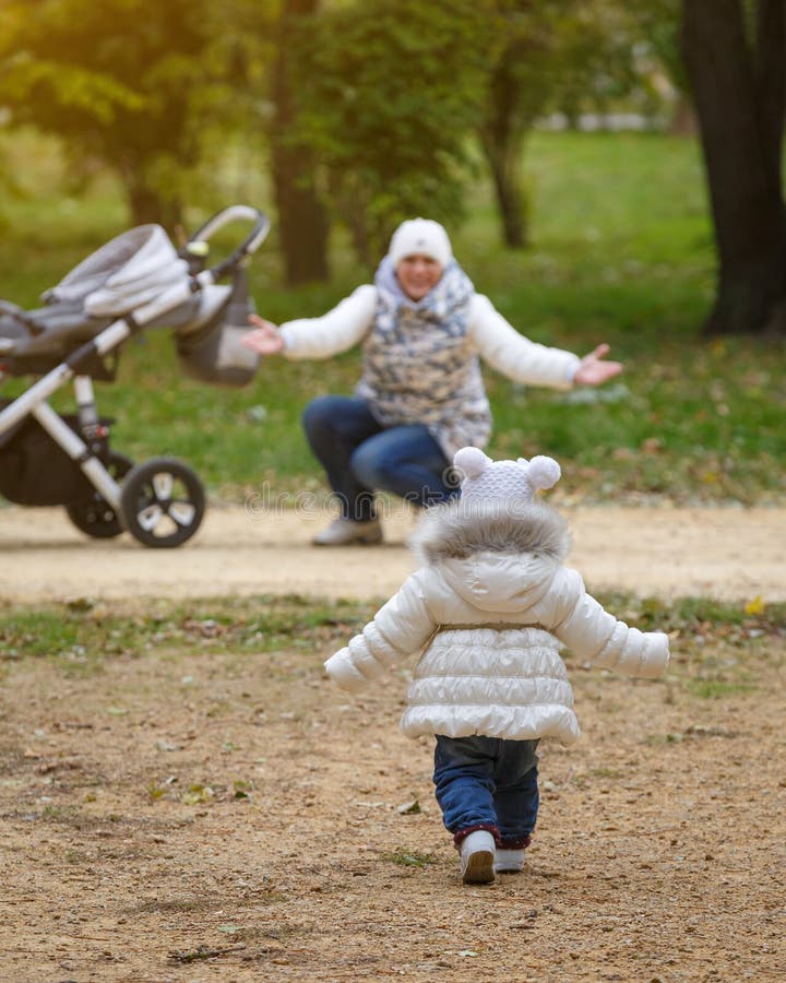 Little girl runs to her mom with a baby stroller in parkland. Mom and daughter reach out to each other stock image Little girl runs to her mom with a baby stroller in parkland. Mom and daughter reach out to each other stock image
