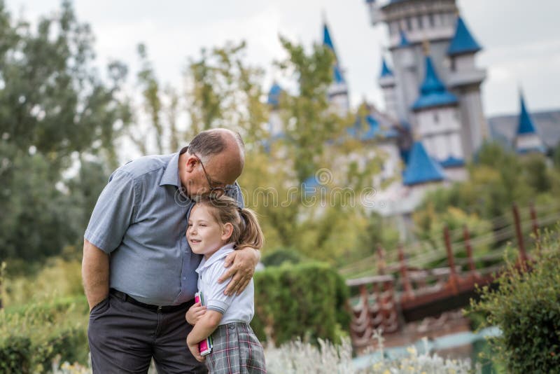 Little Girl with School Uniform and her Grandfather in Green Par