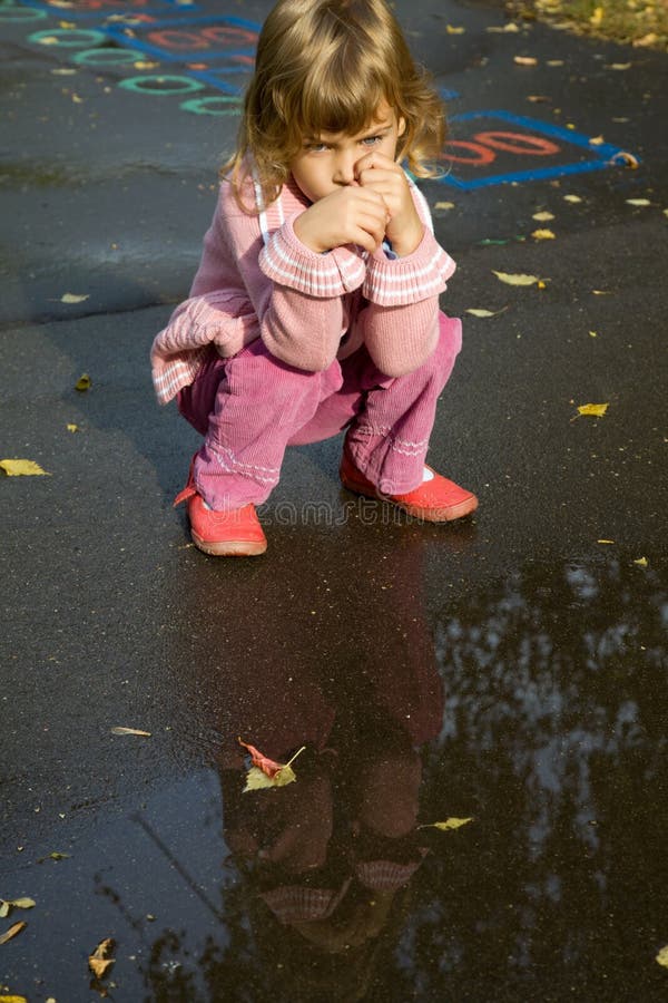 Little girl sit down near pool after rain