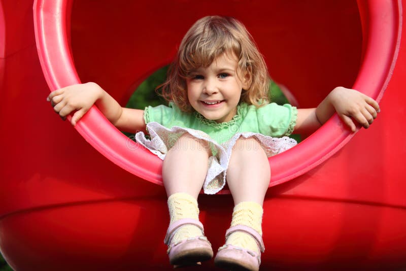 Piccolo ragazza si siede in plastica rossa del foro sul parco giochi.