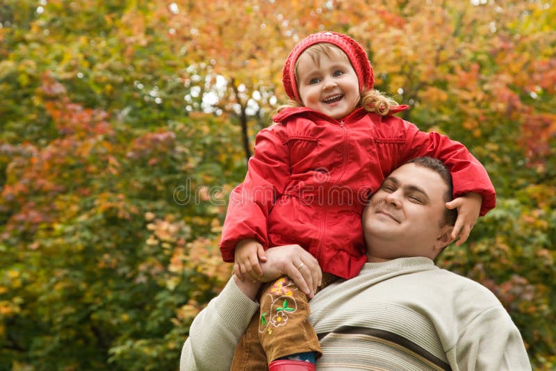 Little girl sits on shoulder at man In park