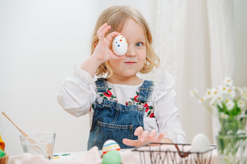 Little girl sitting behind a table with easter eggs, holding one over her eye