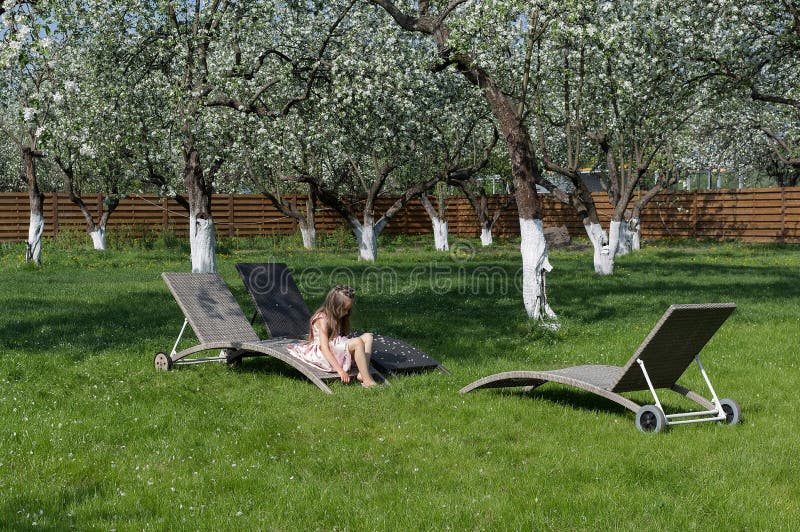 Little girl sitting in blossom apple garden. Relaxing place