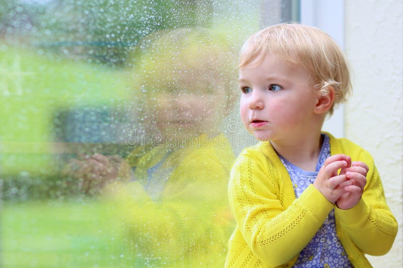 Little girl sitting next window on rainy day