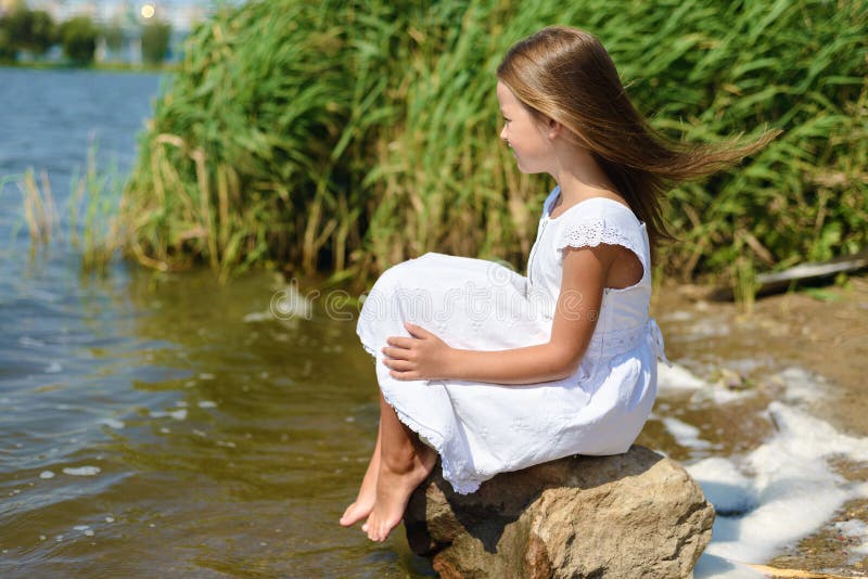 Little girl is sitting on a rock in white dress on sunny day stock photography Little girl is sitting on a rock in white dress on sunny day stock photography