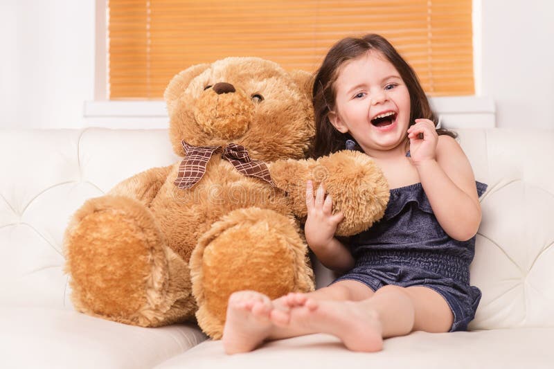 Little girl sitting with teddy bear on sofa.